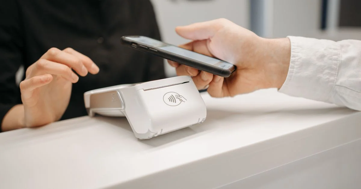 Personne utilisant un smartphone pour un paiement sans contact au comptoir de vente, mettant en avant la commodité sans espèces.