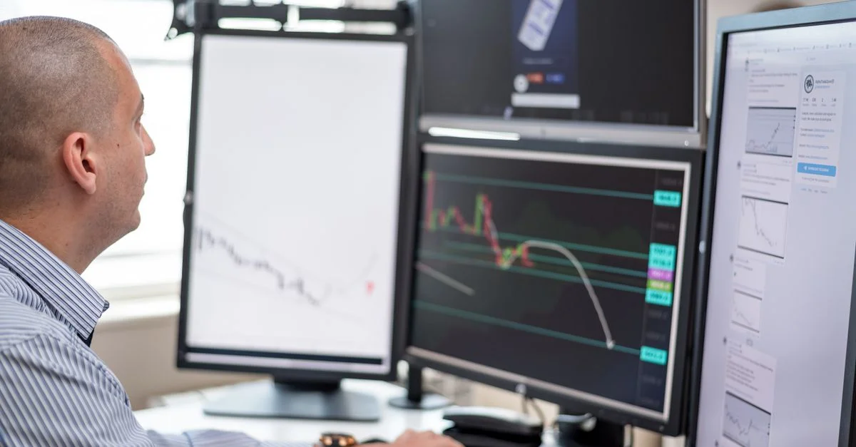 Trader en bourse analysant des graphiques financiers sur plusieurs moniteurs d'ordinateur dans un cadre de bureau.